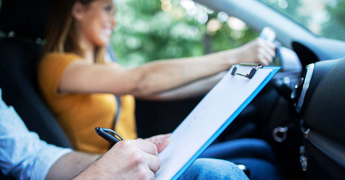 close-up-view-driving-instructor-holding-checklist-while-background-female-student-steering-driving-car